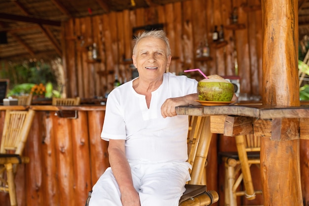 Godersi la pensione. L'uomo anziano felice sta bevendo un'acqua di cocco nel bar della spiaggia.