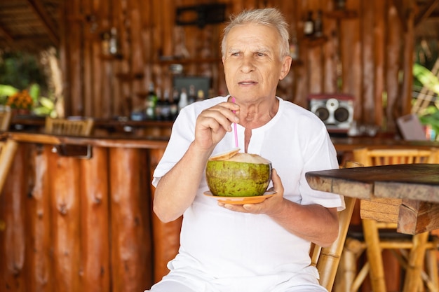 Godersi la pensione. L'uomo anziano felice sta bevendo un'acqua di cocco nel bar della spiaggia.