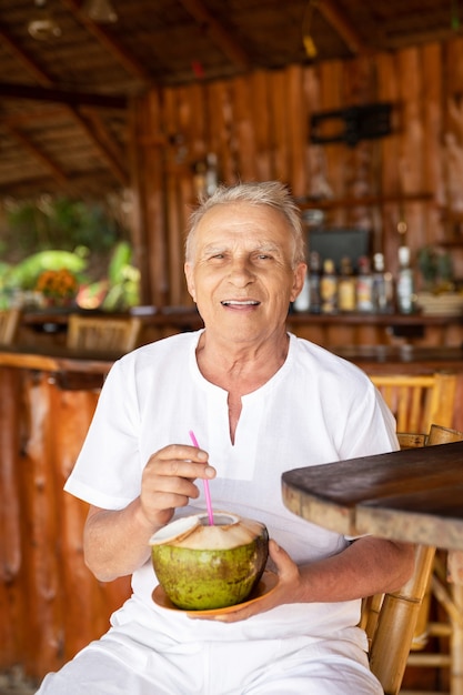 Godersi la pensione. L'uomo anziano felice sta bevendo un'acqua di cocco nel bar della spiaggia.