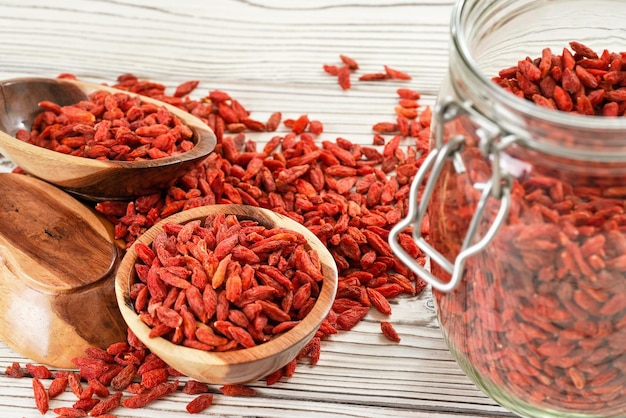 Goji essiccato alias. semi di wolfberry all'interno di una bottiglia di vetro, alcuni in ciotole di legno e versati sulla scrivania di lavagne bianche