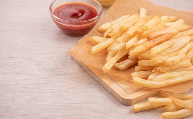 Golden gustose patatine fritte profonde su carta da forno kraft e vassoio da portata da mangiare con ketchup e senape gialla, primi piani, stile di vita.