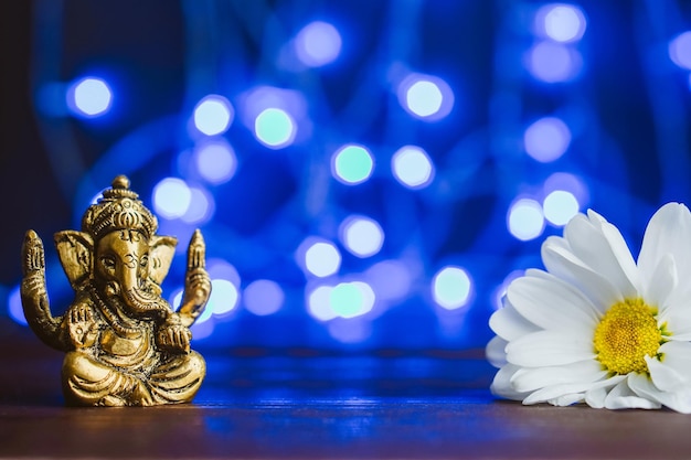 Golden Lord Ganesha scultura e fiore a margherita su sfondo blu illuminato Copia spazio per il testo