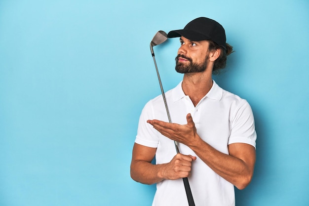Golfista barbuto dai capelli lunghi che tiene un club da golf in uno studio blu