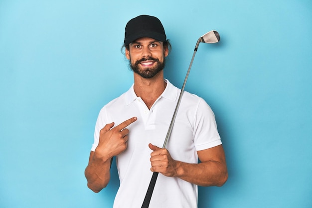 Golfista dai capelli lunghi con club e cappello sorridente e puntando da parte mostrando qualcosa nello spazio vuoto
