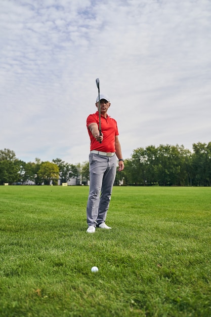 golfista maschio concentrato che tiene la sua mazza da golf di ferro di fronte a lui