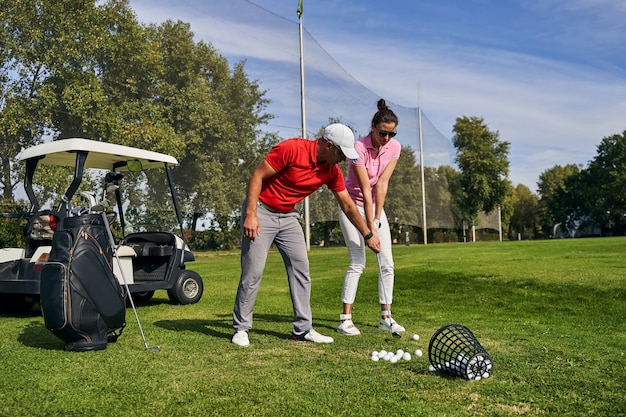 Golfista principiante femminile caucasica concentrato che pratica una tecnica di colpo di puttana supportata da un allenatore professionista