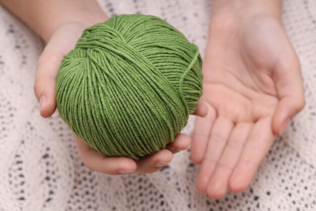 Gomitolo di lana verde nelle mani sullo sfondo di una tovaglia a maglia bianca. Foto di alta qualità