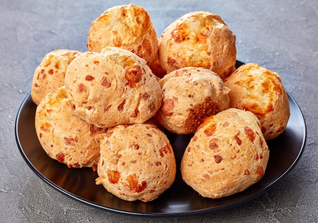 Gougeres croccanti deliziosi, palle di bignè al formaggio su un piatto nero. Tradizionale francese choux panini al formaggio su un tavolo di cemento, vista dall'alto, close-up