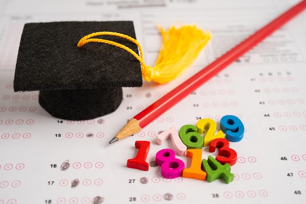 Graduation gap hat and pencil on answer sheet paper Test di studio sull'istruzione Concetto di insegnamento dell'apprendimento