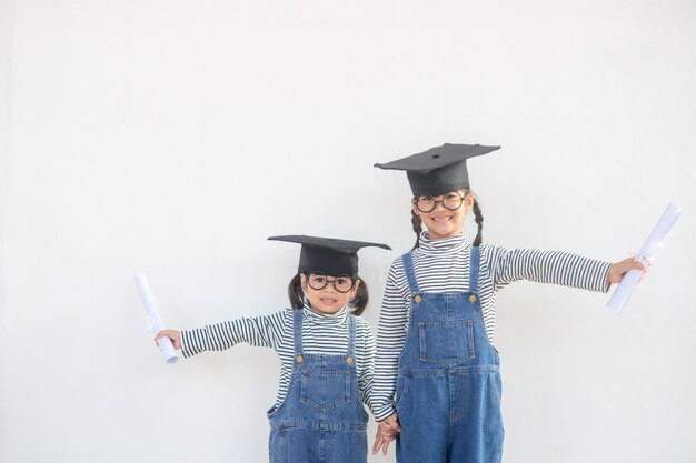 Graduazione della ragazza dei bambini dei fratelli germani con la protezione ed il diploma sopra bianco.