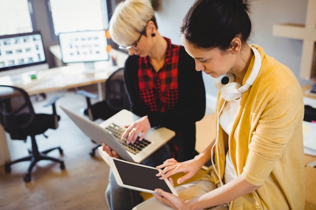 Grafico femminile due che per mezzo della compressa e del computer portatile digitali