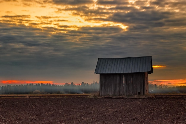 Granaio su un campo agricolo contro un cielo nuvoloso durante il tramonto