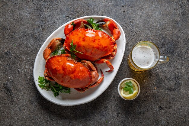 Granchi cucinati interi su un piatto bianco con limone e birra sullo sfondo di cemento grigio