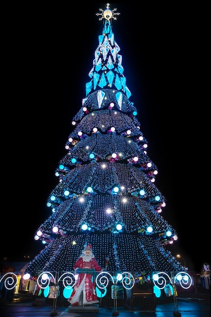 grande albero di Natale scintillante della città di notte con Babbo Natale alla base