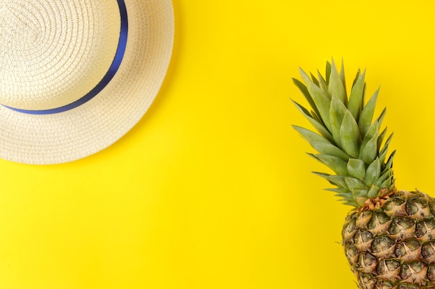 Grande ananas di frutta matura e cappello estivo su un tavolo giallo brillante. estate. vista dall'alto.