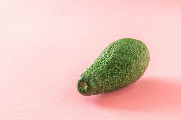 Grande avocado verde maturo bello su sfondo rosa. Deliziosa verdura tropicale.