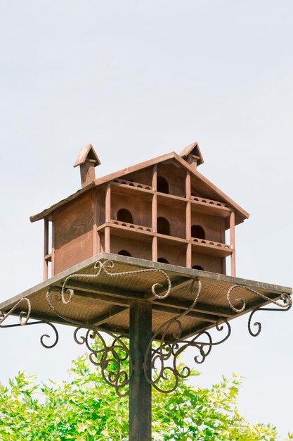 Grande birdhouse in legno su un palo di metallo contro il cielo e alberi verdi