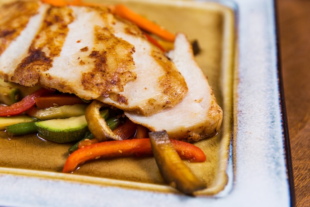 Grande bistecca di pollo con le verdure sul piatto quadrato sulla tavola di legno in ristorante di lusso