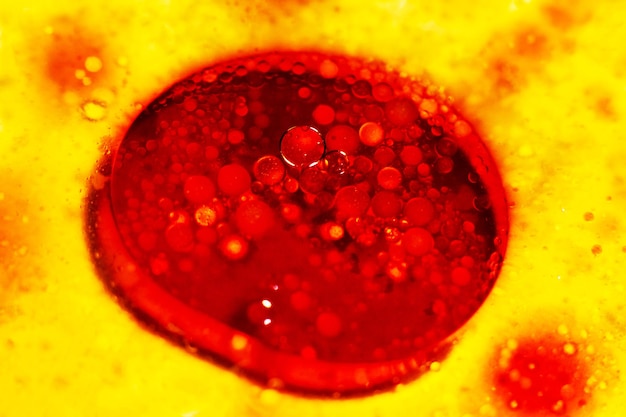 Grande bolla rossa brillante con piccole bolle che galleggiano sulla superficie dell'olio di molecola di batterio liquido giallo