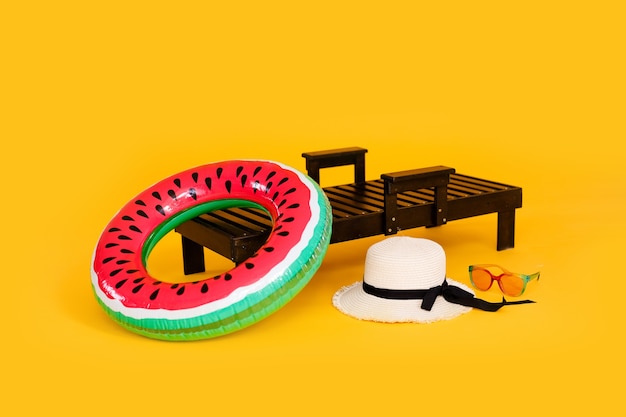 Grande cappello e occhiali da sole sulla sdraio in legno isolato su sfondo giallo. Concetto di vacanze estive.