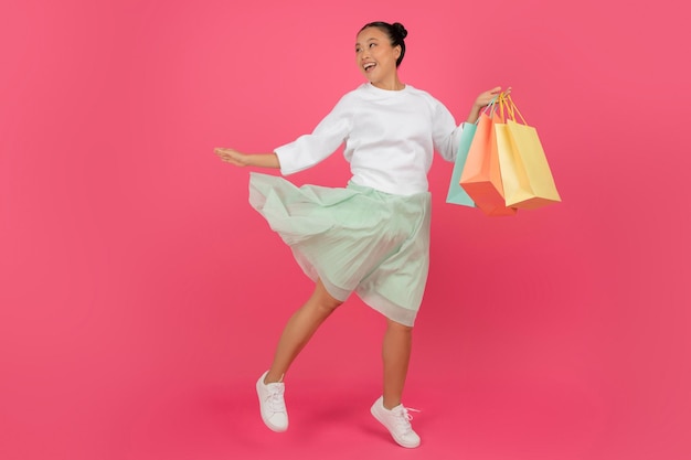 Grande concetto di vendita giovane donna asiatica felice che corre con borse da shopping colorate