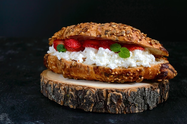 Grande croissant ai cereali con ricotta e fragole fresche su uno sfondo scuro