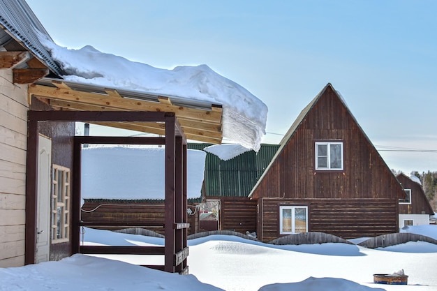 Grande cumulo di neve sul tetto della casa rurale la neve accumulata durante l'inverno scivola dal tetto della casa di legno