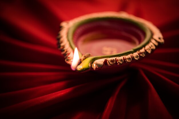 Grande diwali diya illuminato o lampada di argilla posizionata su un panno di raso che crea effetti di raggi in tessuto, illuminazione lunatica, messa a fuoco selettiva