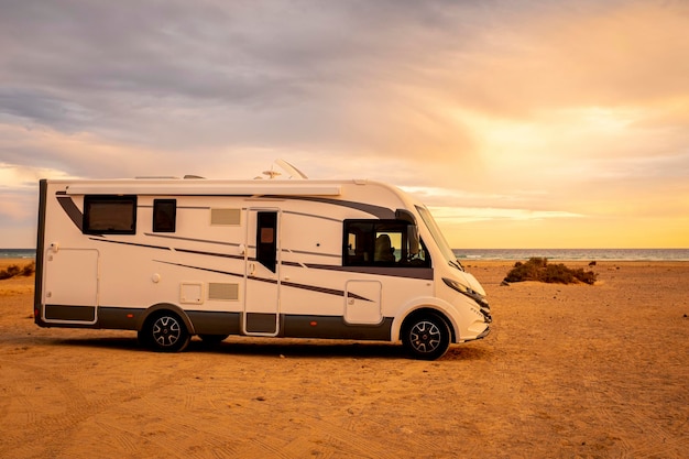 Grande e moderno camper camper parcheggiato a terra e bellissima spiaggia con mare e luci del tramonto sullo sfondo. Concetto di vacanza estiva di viaggio con camper gratuito