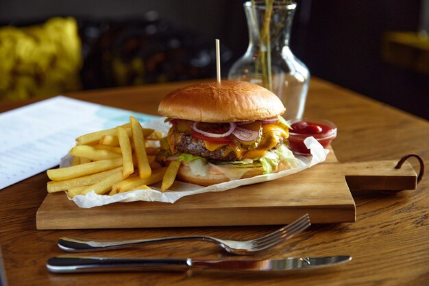 Grande e succoso hamburger con patatine fritte su una tavola di legno