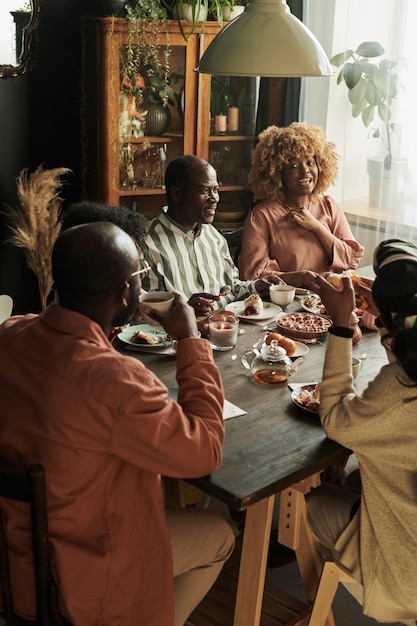 Grande famiglia africana seduta al tavolo e parlando per una tazza di tè e una torta nella sala da pranzo