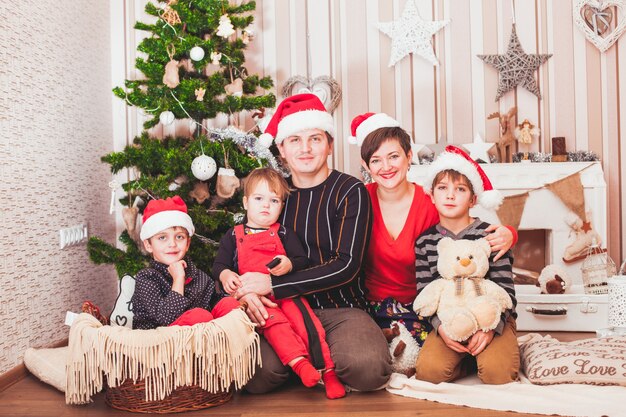 Grande famiglia allegra che indossa il cappello di Babbo Natale seduto all'interno di una casa decorata per Natale