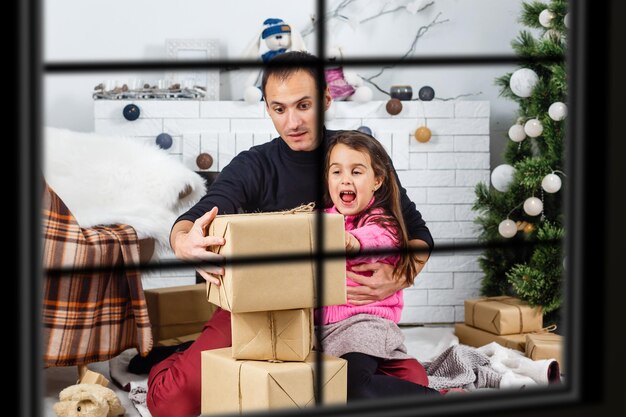 Grande famiglia con tre bambini che festeggiano il Natale a casa. Cena festiva al camino e all'albero di Natale. Genitori e bambini che mangiano al caminetto nella stanza decorata. Candela della corona di avvento di illuminazione del bambino.