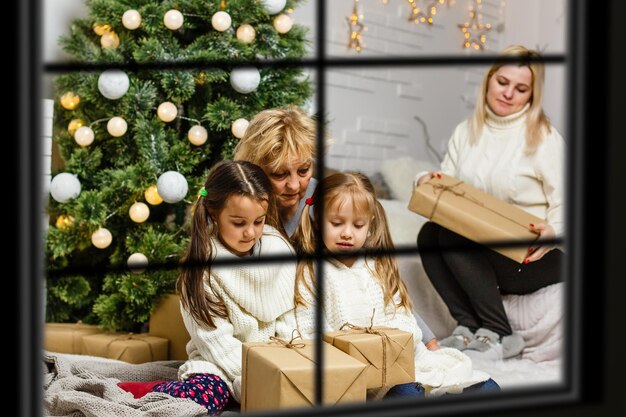 Grande famiglia con tre bambini che festeggiano il Natale a casa. Cena festiva al camino e all'albero di Natale. Genitori e bambini che mangiano al caminetto nella stanza decorata. Candela della corona di avvento di illuminazione del bambino.