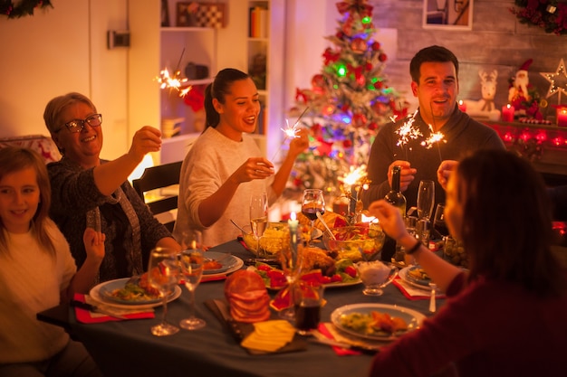 Grande famiglia felice che canta alla festa di natale con cibo delizioso e fuochi d'artificio a mano.