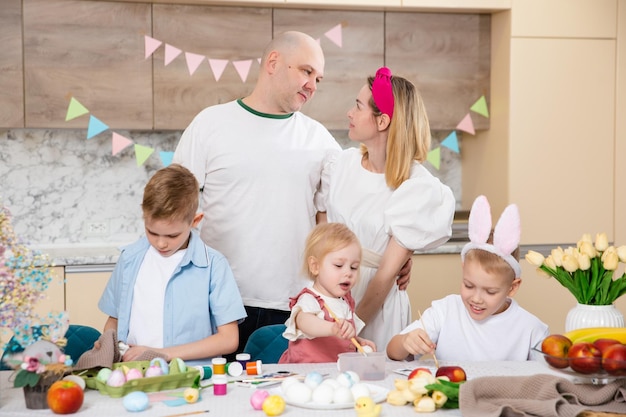 Grande famiglia felice che si prepara per la Pasqua Bambini carini che dipingono le uova Attività domestiche Concetto di unità e amore Mamma papà figlio figlia Fratelli e sorelle