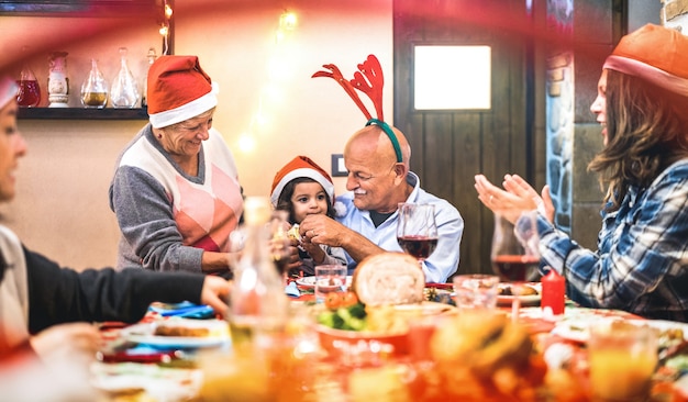 Grande famiglia multigenerazionale che si diverte alla cena di Natale - Concetto di vacanza invernale x mas con genitori e figli che mangiano insieme aprendo i regali a casa - Focus sulle mani del nonno e della figlia