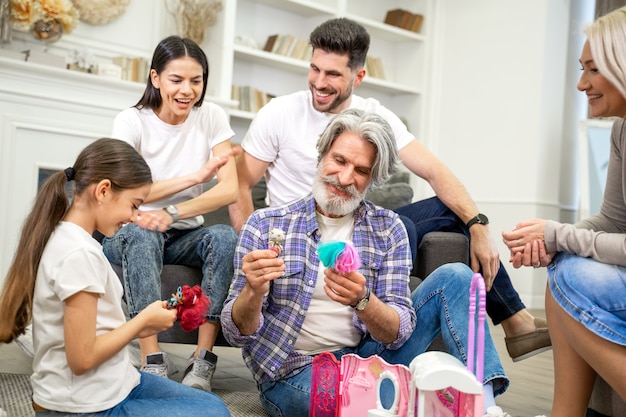 grande famiglia multigenerazionale felice che gioca con una bambina carina che guarda la nuova casa delle bambole