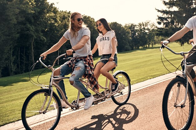 Grande giornata con gli amici. Gruppo di giovani felici in abbigliamento casual che sorridono mentre vanno in bicicletta insieme all'aperto