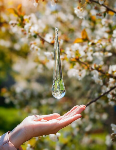 Grande goccia trasparente sullo sfondo di un frutteto di mele in fiore con una mano Il concetto di protezione dell'acqua ecologia del pianeta