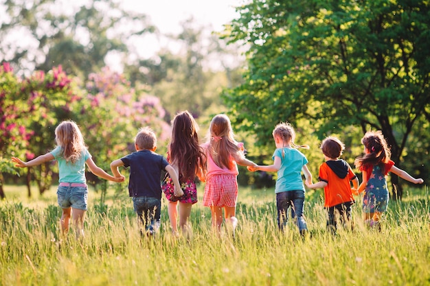 Grande gruppo di bambini, amici ragazzi e ragazze che corrono nel parco sulla soleggiata giornata estiva in abiti casual.