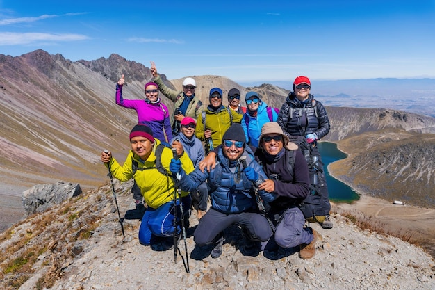 Grande gruppo di persone che si divertono in posa di successo sulla cima di una montagna contro laghi e montagne