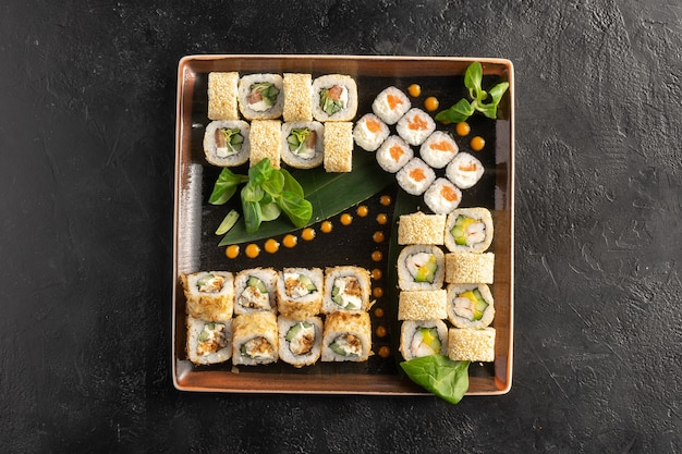 Grande maki sushi set con un vario assortimento di panini giapponesi in un piatto quadrato su un tavolo di pietra nera