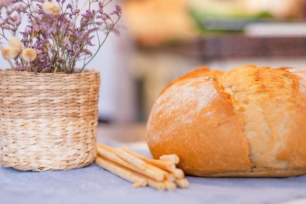 Grande pagnotta di pane sul tavolo di casa. Grissini, cesto di fiori secchi