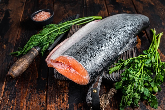 Grande pezzo di pesce salmone tagliato crudo su un tagliere di legno con coltello da chef