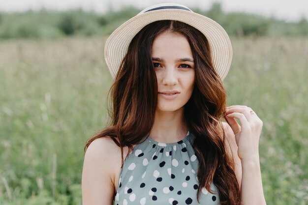 Grande ritratto di una giovane ragazza con un cappello di paglia in un campo verde estivo