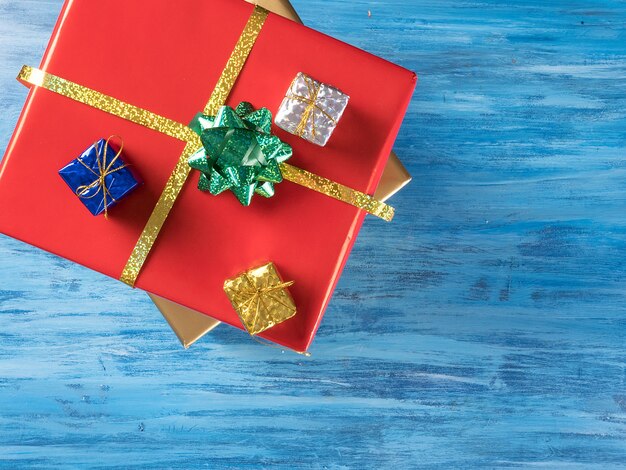 Grande scatola regalo di Natale rossa con scatole più piccole su fondo di legno vintage blu. Simbolo di celebrazione.