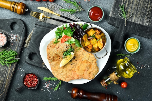 Grande schnitzel di pollo fritto con verdure in un piatto su uno sfondo di pietra nera Foto di cibo
