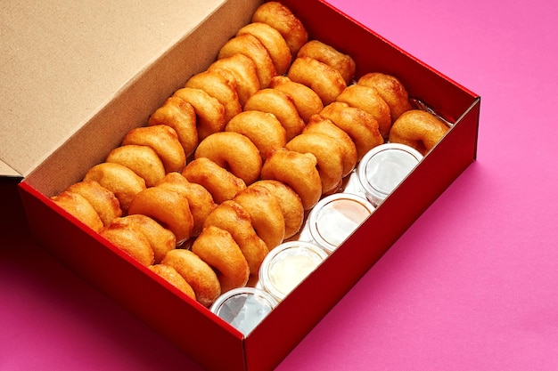 Grande set di ciambelle in una scatola con vari condimenti dolci su sfondo rosa.