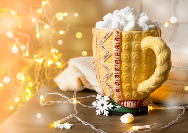 Grande tazza con bevanda calda e marshmallow sullo sfondo delle luci di Natale.